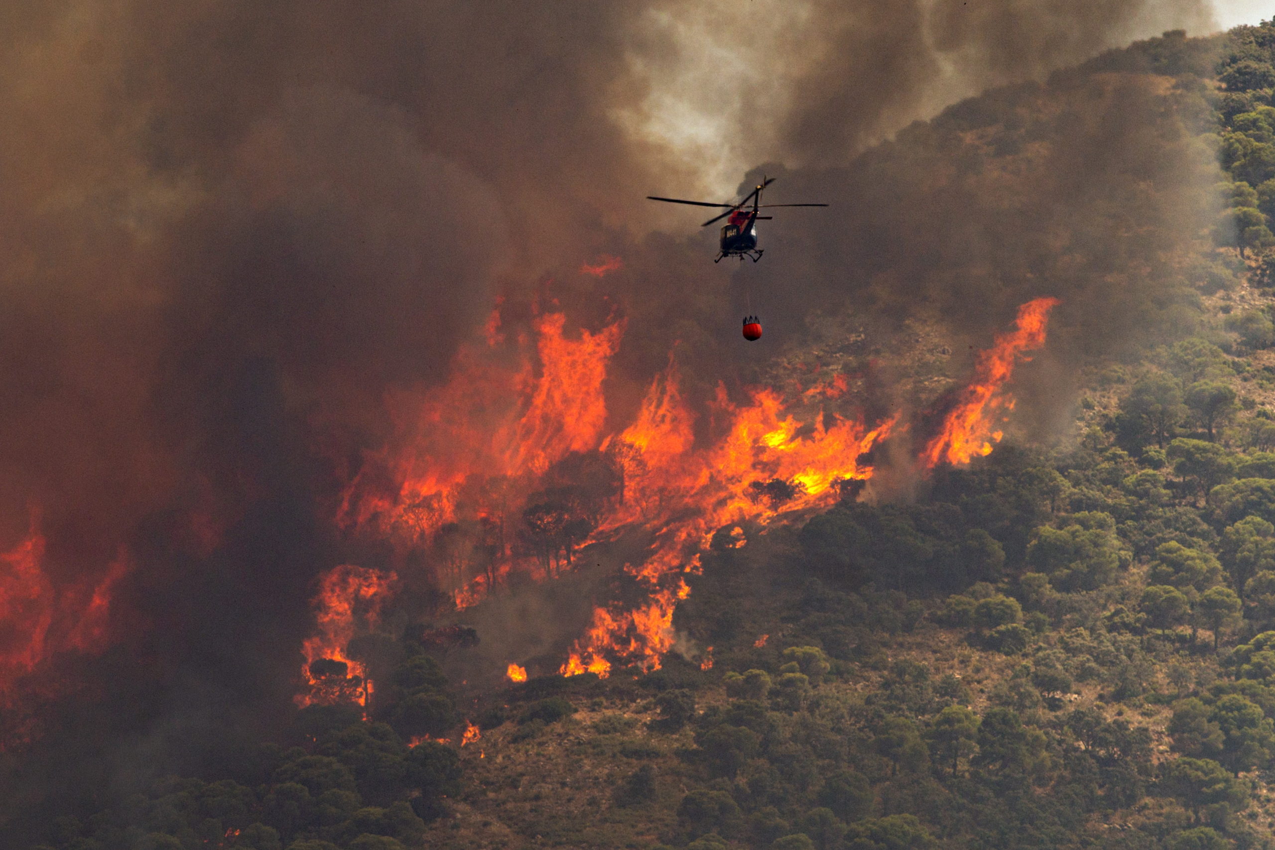 epa10072820 A helicopter pours water into the flames of a forest fire in Mijas, Malaga, southern Spain, 15 July 2022. Regional authorities activated the first level of the Emergency Plan for Forest Fire Emergencies as the fire has been spreading since noon and some residential areas have already been evacuated. EPA-EFE/DANIEL PEREZ